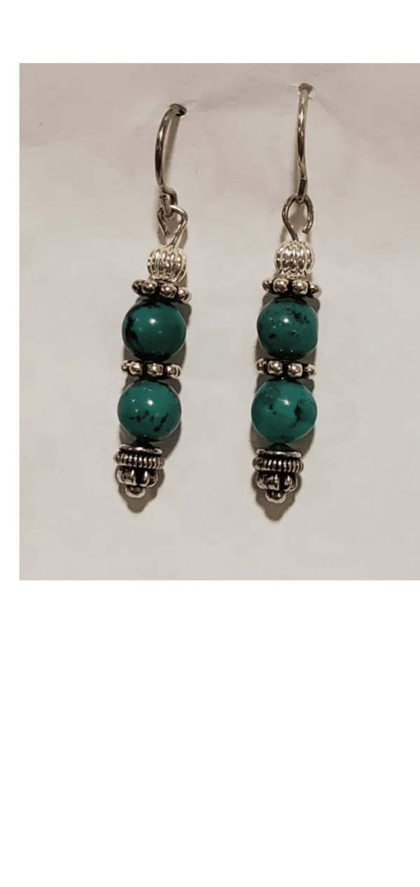 The Blue Bells feature two dangling earrings with turquoise beads and ornate silver embellishments, set against a white background.